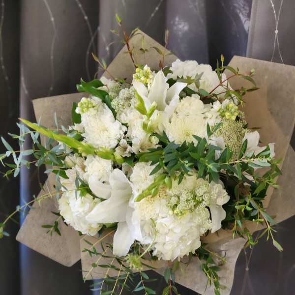 Hand-tied bouquet of white lilies and hydrangeas wrapped in brown kraft paper