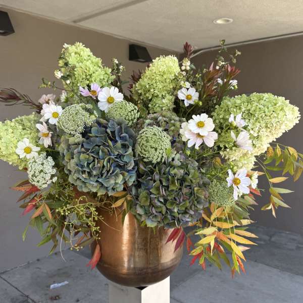 Large floral arrangement with green hydrangeas, white daisies, and a copper vase