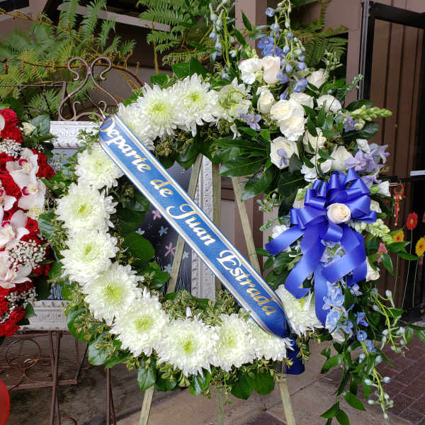 Large funeral wreath with white flowers and a blue memorial ribbon