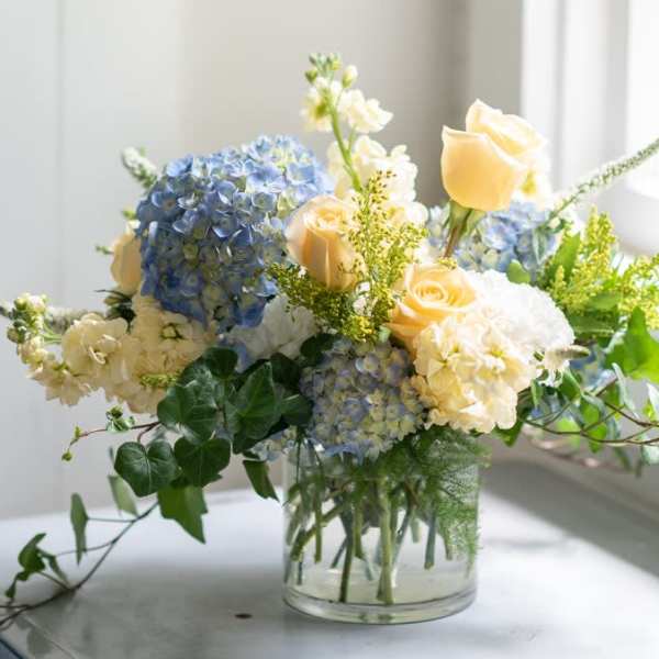 Blue hydrangeas and pale yellow roses in a clear glass vase