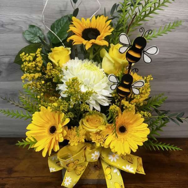 Yellow floral arrangement with sunflowers, roses, and a bee decoration