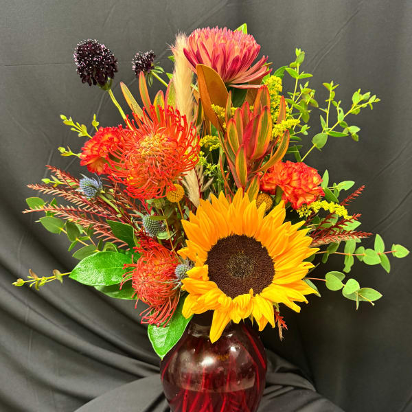 Bright mixed bouquet with a sunflower in a red glass vase
