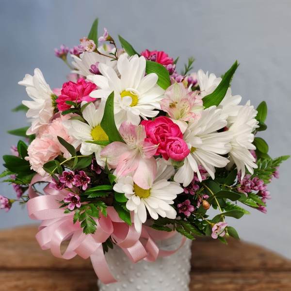 White daisies and pink blooms in a white textured vase with a pink ribbon bow.