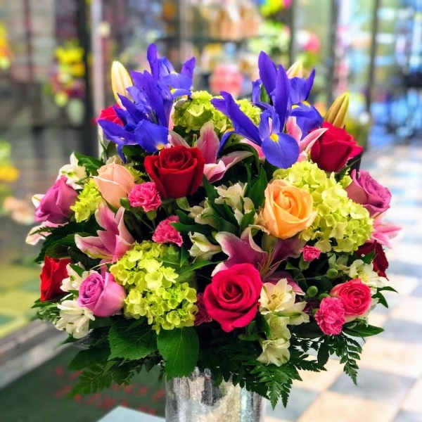 Tall mixed bouquet of roses, lilies, irises, and hydrangeas in a silver glass vase