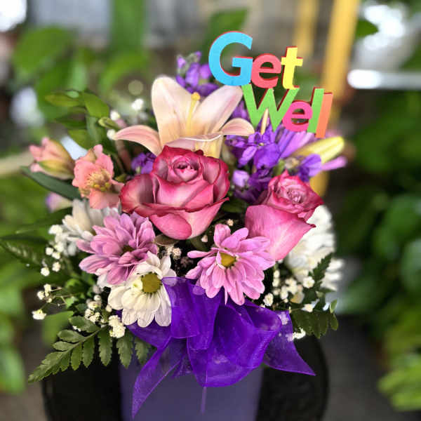 Pink roses and daisies in a purple container with a Get Well sign