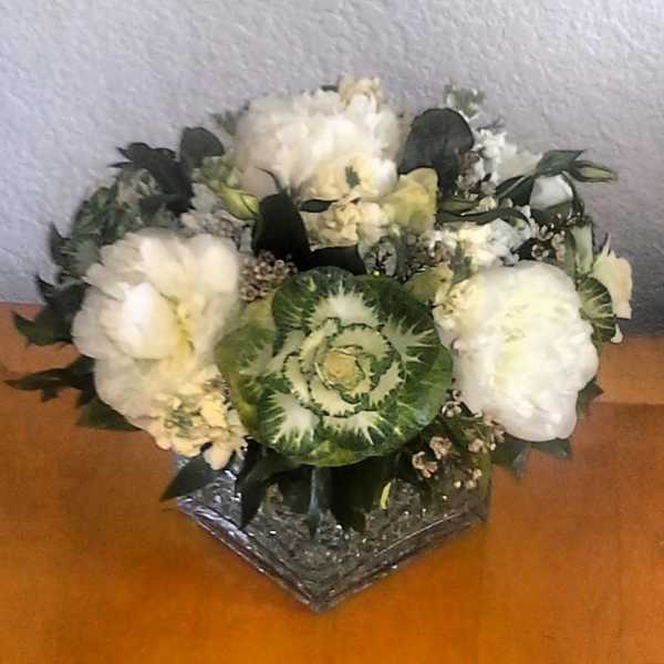 White floral arrangement with a green ornamental cabbage center in a glass vase