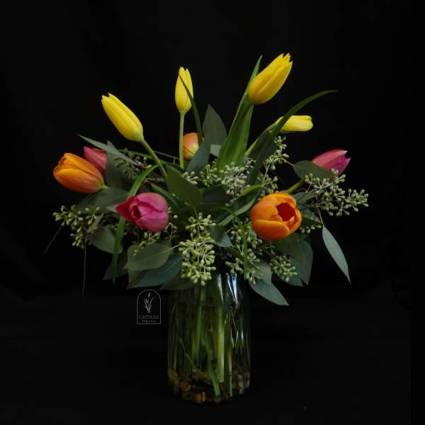 Bouquet of yellow, pink, and orange tulips in a clear glass vase