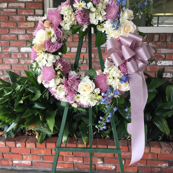 Floral wreath on an easel with pink, white, and blue flowers and a lavender ribbon