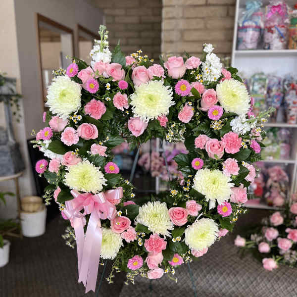 Heart-shaped floral wreath with pink roses and white chrysanthemums on an easel