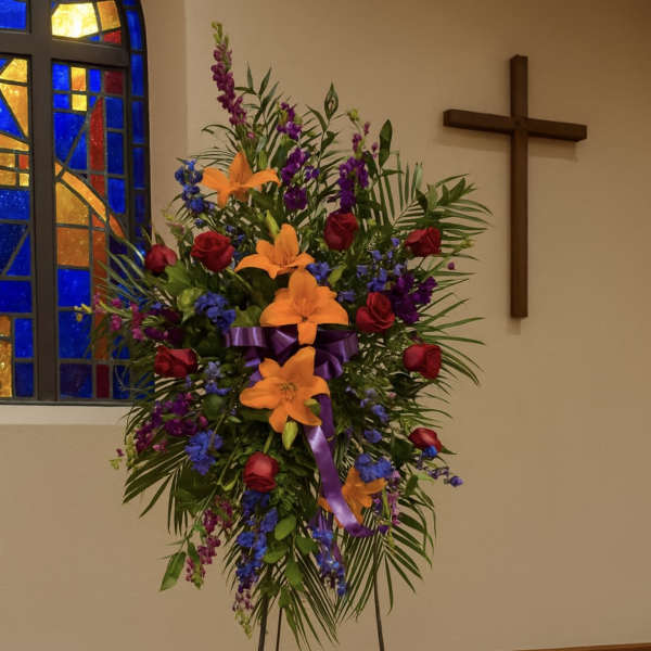 Standing floral spray with lilies, roses, and purple flowers on an easel