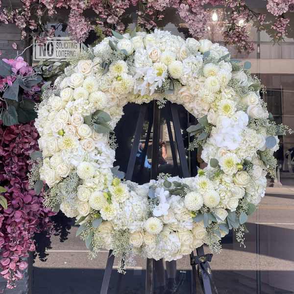 Large white floral wreath on a black stand with roses and dahlias