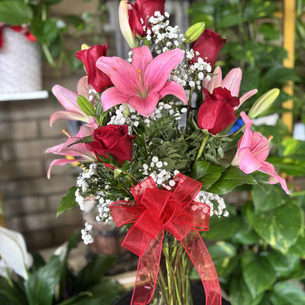 Pink lilies and red roses in a glass vase with a red ribbon