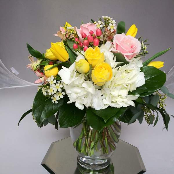 Bouquet of yellow and pink roses with white flowers in a clear glass vase