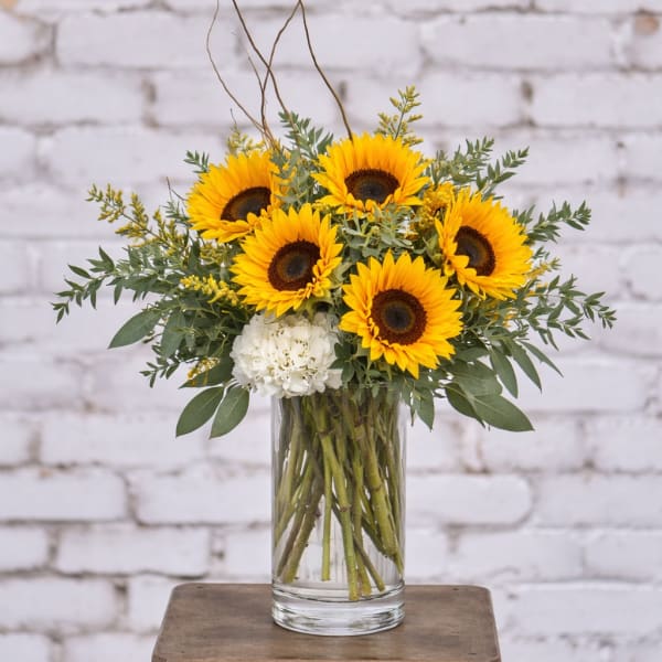 Sunflower arrangement in a clear glass vase with white accent blooms