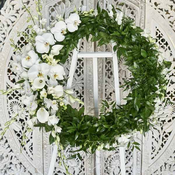 White floral wreath with orchids and greenery on a stand