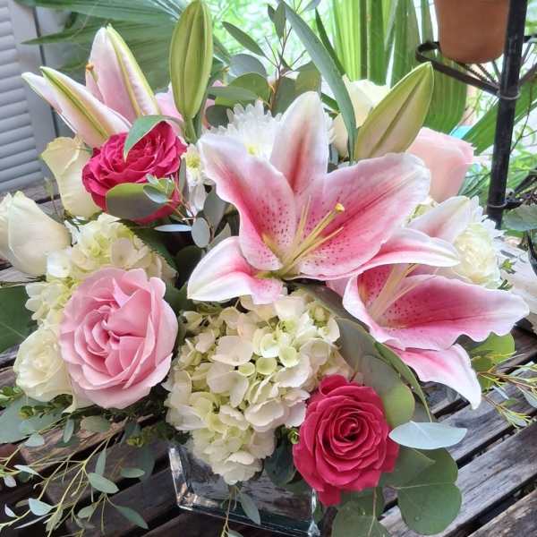 Pink lilies and roses arranged in a square glass vase