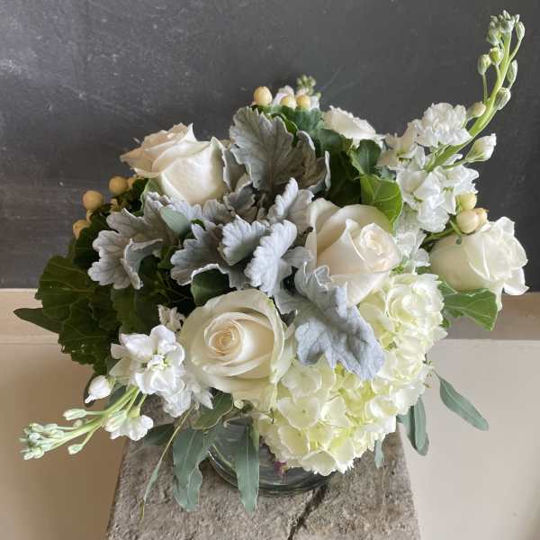 White roses and hydrangeas in a glass vase with silver foliage