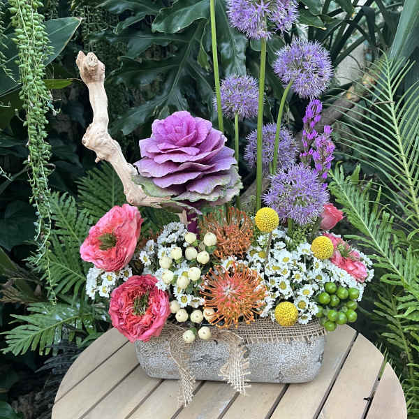 Mixed floral arrangement in a stone container with purple, pink, and white blooms