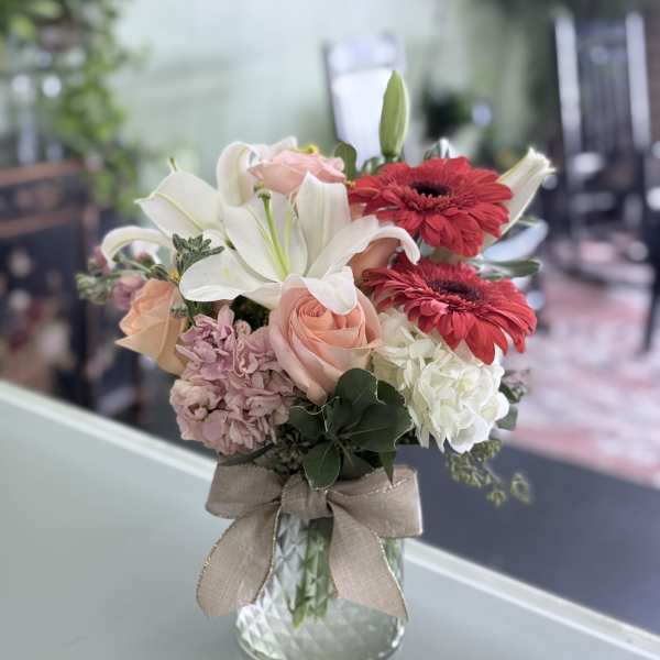 Bouquet of lilies, roses, and gerbera daisies in a glass vase with a ribbon