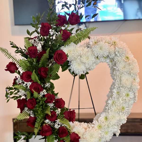 Heart-shaped floral wreath with red roses and white chrysanthemums on an easel