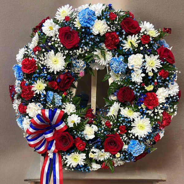 Circular wreath of red, white, and blue flowers with a ribbon bow