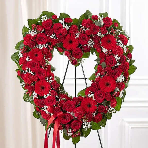Heart-shaped red floral wreath on a stand with a ribbon bow