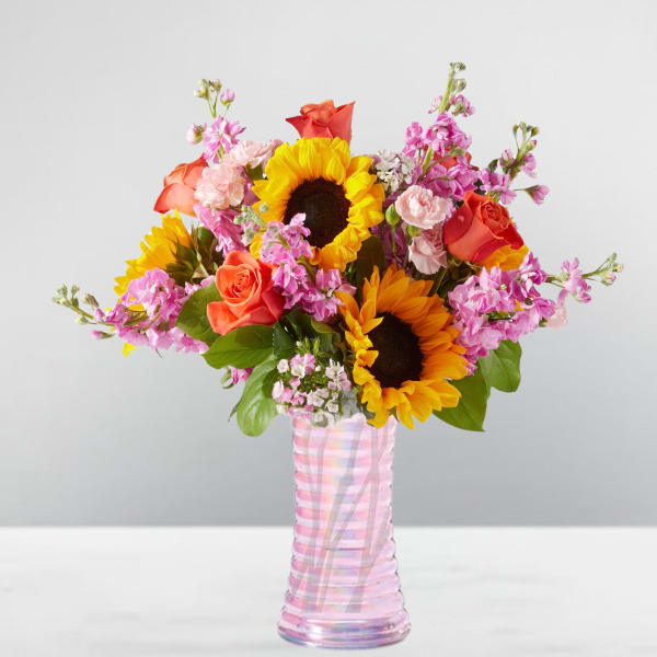 Bouquet of sunflowers, roses, and pink flowers in a striped glass vase