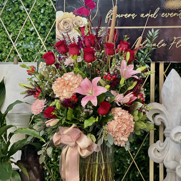 Tall bouquet of red roses and pink lilies in a glass vase with a ribbon
