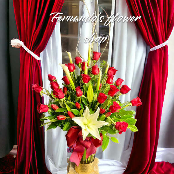 Tall arrangement of red roses and white lilies in a glass vase with red ribbon bow
