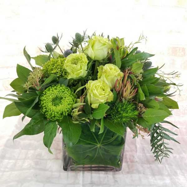 Green floral arrangement in a square glass vase with pale roses and chrysanthemums