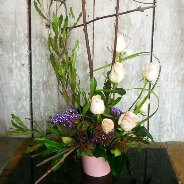 Tall floral arrangement with white roses and purple accents in a pink vase