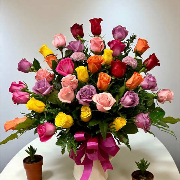Colorful bouquet of roses in a white vase with a pink ribbon