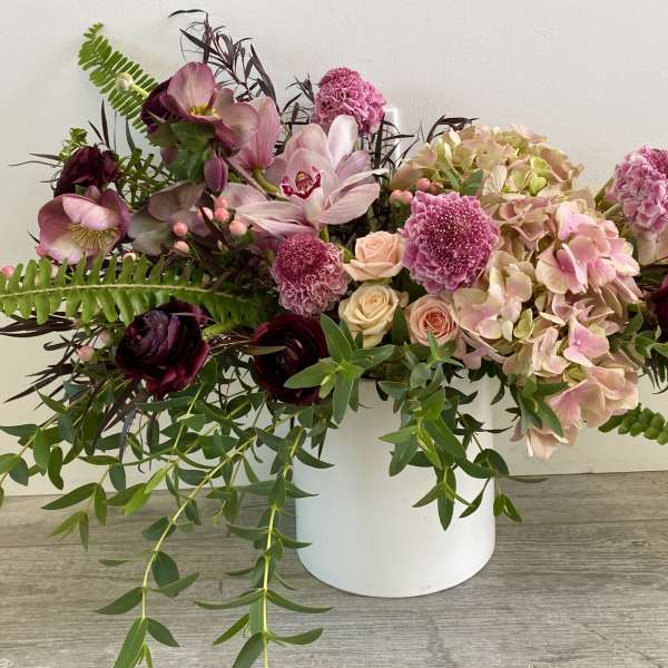Pink and burgundy floral arrangement in a white container