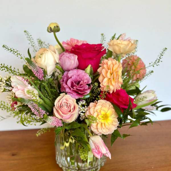 Mixed bouquet of pink, peach, and red flowers in a clear glass vase