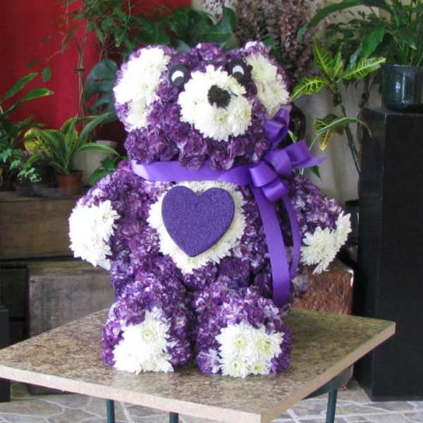 Purple and white teddy bear made of flowers with a ribbon bow