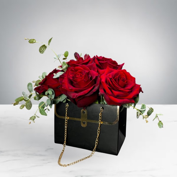 Red roses arranged in a black handbag-style box with gold chain handles
