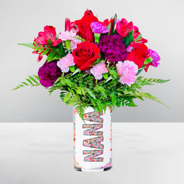 Mixed bouquet of red roses and pink blooms in a white patterned cylinder vase