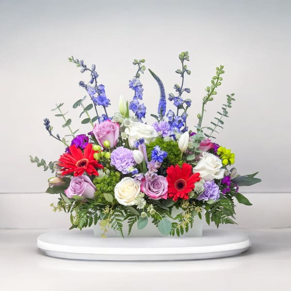 Mixed bouquet in a rectangular vase with roses, gerberas, and blue spikes