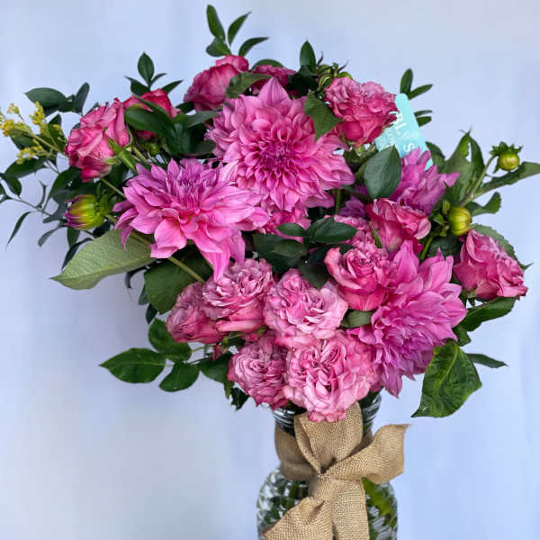 Pink flowers arranged in a glass vase with a burlap bow
