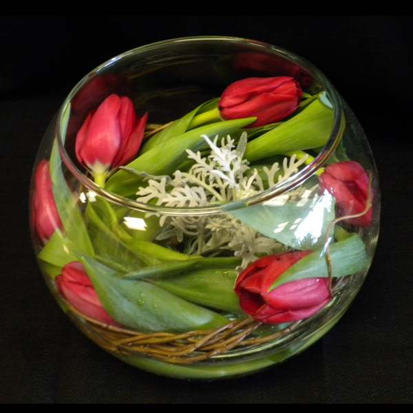 Pink tulips arranged in a round glass bowl with decorative foliage
