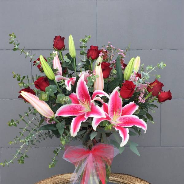 Bouquet of pink lilies and red roses in a glass vase with a pink ribbon