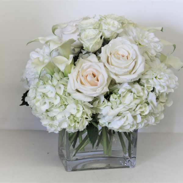 White roses and hydrangeas arranged in a clear square vase