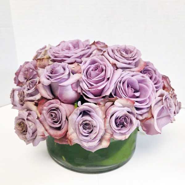 Lavender roses arranged in a low green glass vase
