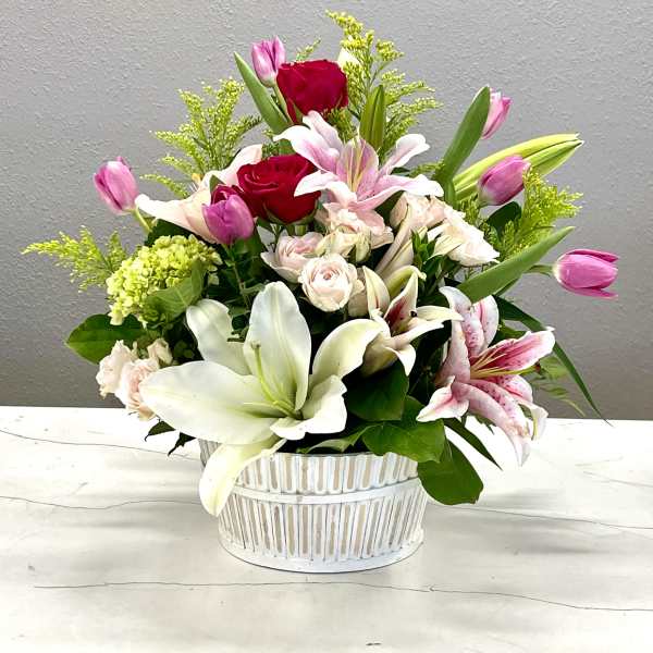 Mixed bouquet of lilies, roses, and tulips in a white basket