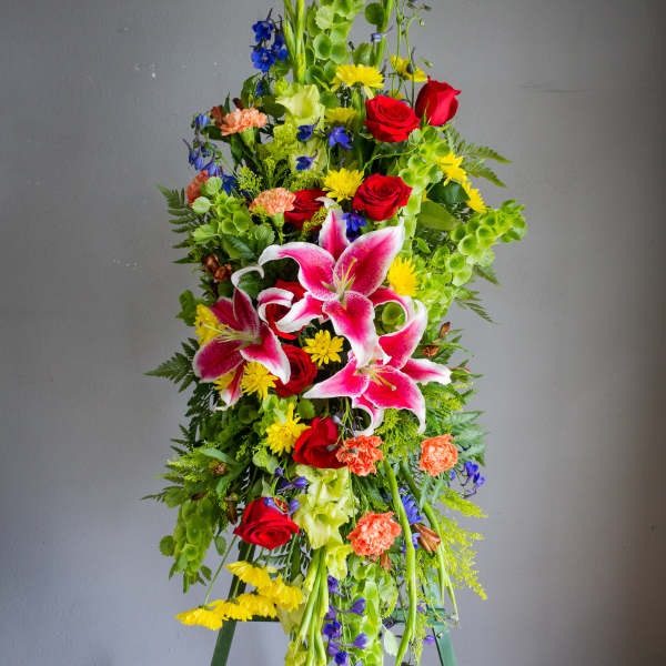 Tall standing floral spray with pink lilies, red roses, and bright mixed blooms