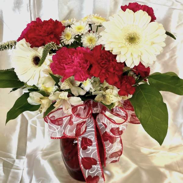 Bouquet of red and white flowers in a red vase with a heart ribbon