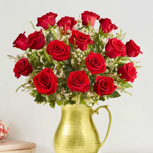 Arrangement of red roses with small white blooms in a hammered gold metal pitcher.