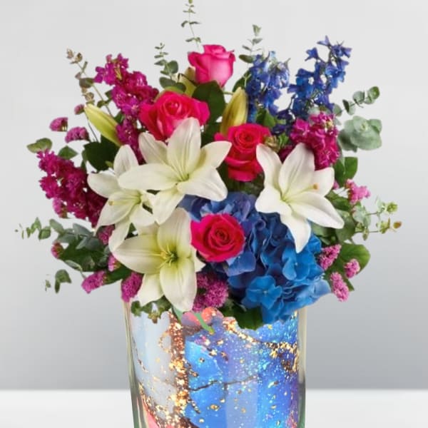 Bouquet of pink roses, white lilies, and blue hydrangeas in a glass vase