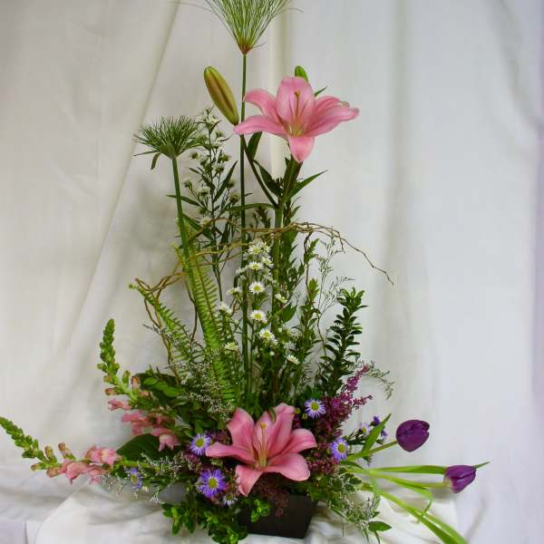 Tall floral arrangement with pink lilies and purple tulips in a dark container
