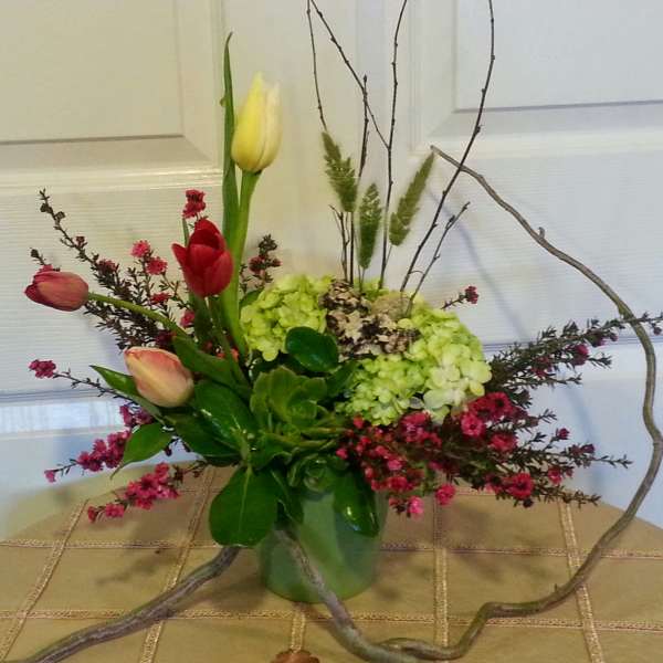 Mixed tulips and hydrangeas in a glass vase with curly branches